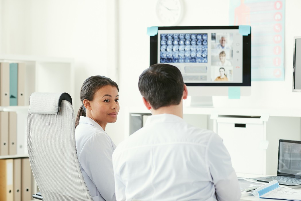 Médicos analisando imagens de ressonância magnética em videoconferência, discutindo protocolos de segurança do paciente em exames de imagem