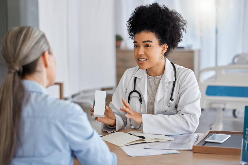 Médica conversa com paciente em consultório durante orientação de saúde, com estetoscópio, anotações e materiais sobre a mesa, ilustrando artigo sobre doenças que o cigarro causa