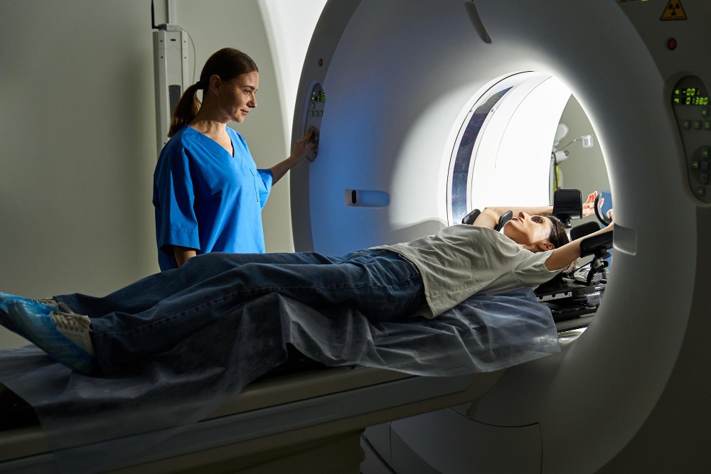  Paciente deitada em maca entrando em equipamento de ressonância, acompanhada por profissional de saúde ao lado do aparelho, ilustrando artigo sobre dor na lombar.