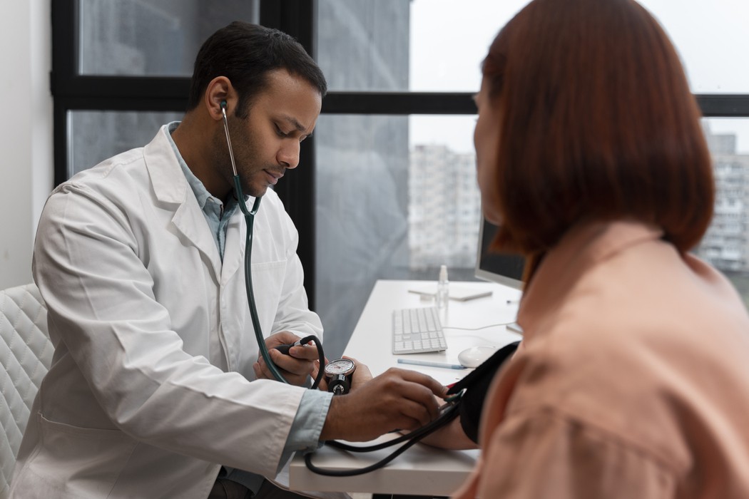 Médico medindo a pressão arterial de paciente em consultório, com estetoscópio e esfigmomanômetro, ilustrando conteúdo sobre exames laboratoriais de rotina