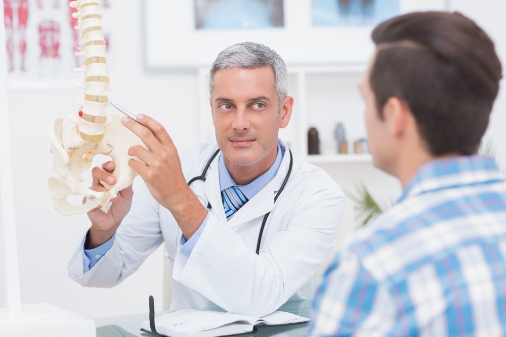 Imagem de médico explicando estrutura óssea e possíveis causas de dor na coluna a um paciente ilustrando artigo sobre ortopedista em Porto Alegre