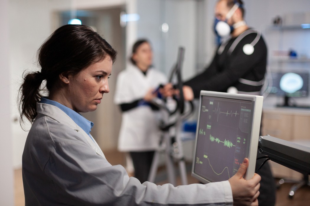 Médica observa monitor com traçado de eletrocardiograma durante teste ergométrico em elíptico, exame utilizado para investigar palpitação no coração