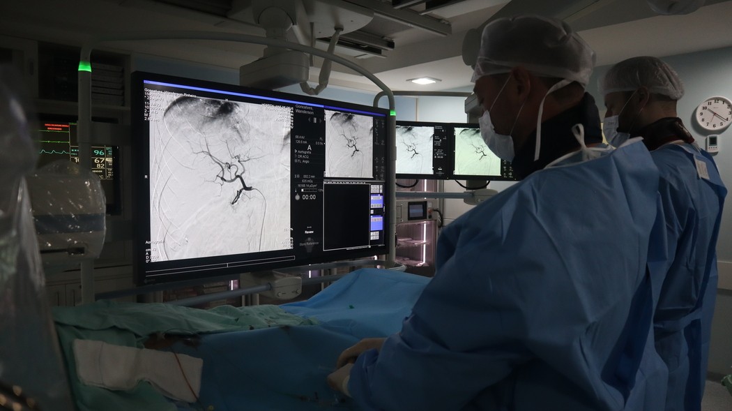 Equipe médica observa imagens vasculares em monitores durante procedimento em sala hospitalar equipada com tecnologia de radiologia intervencionista, ilustrando artigo sobre radiologia intervencionista tratamentos.