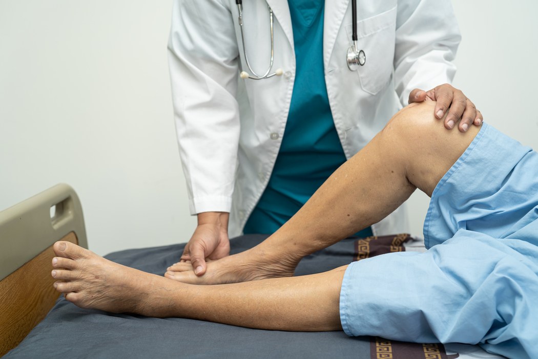 Médico realiza exame físico na perna de um paciente para investigar dor, alterações circulatórias e possíveis sinais relacionados à trombose.