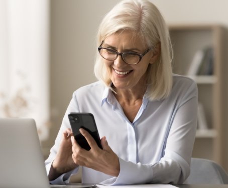 Mulher sentada frente uma mesa, sorrindo e com smartphone na mão