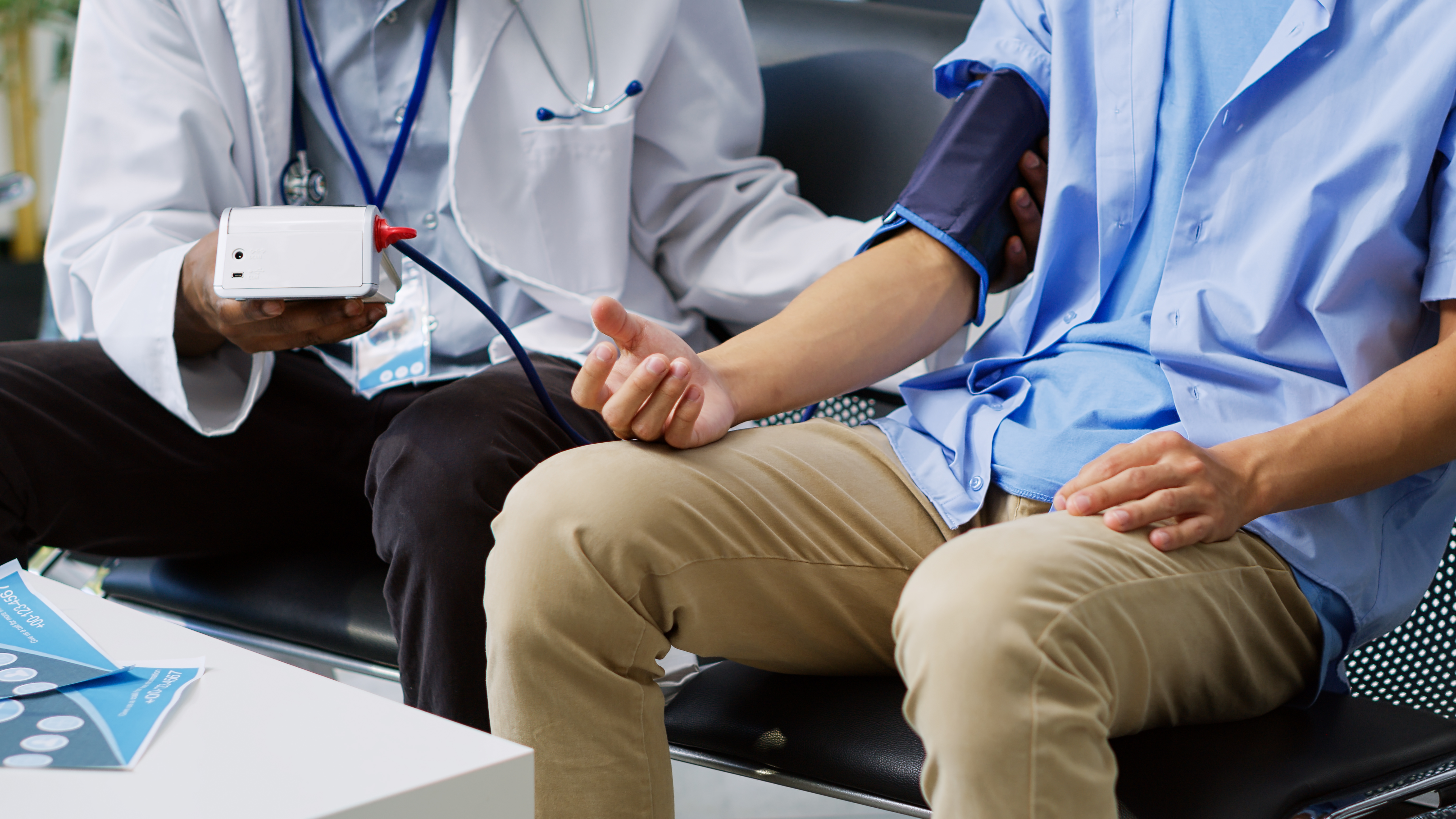 Physician using medical tonometer to measure patient pulse pressure and hypertension in hospital waiting area. African american medic doing cardiology exam with asian man during checkup visit